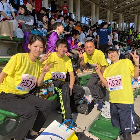 リレーマラソン大会で4人の社員が黄色いTシャツを着て笑顔でピースサインをしている画像