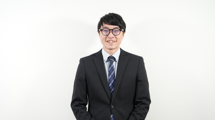 メガネをかけてスーツを着た男性社員がカメラに向かって笑顔で微笑んでいる様子