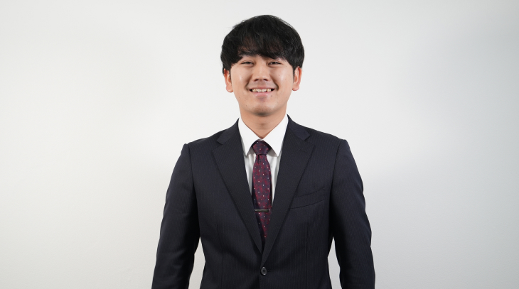 スーツを着た男性社員がカメラに向かって笑顔で微笑んでいる様子