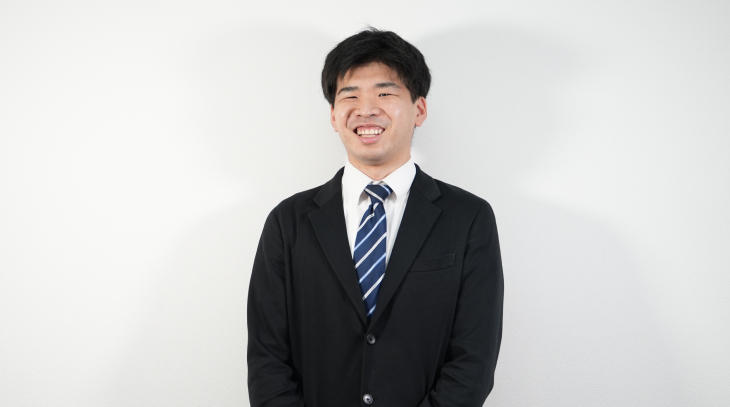 スーツを着た男性社員がカメラに向かって笑顔で微笑んでいる様子