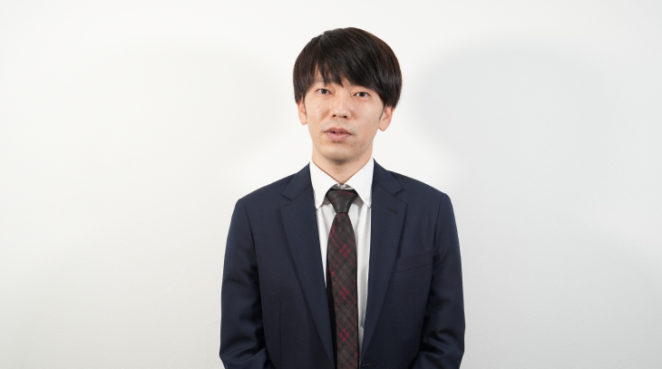 スーツを着た男性社員がカメラに向かって微笑んでいる様子